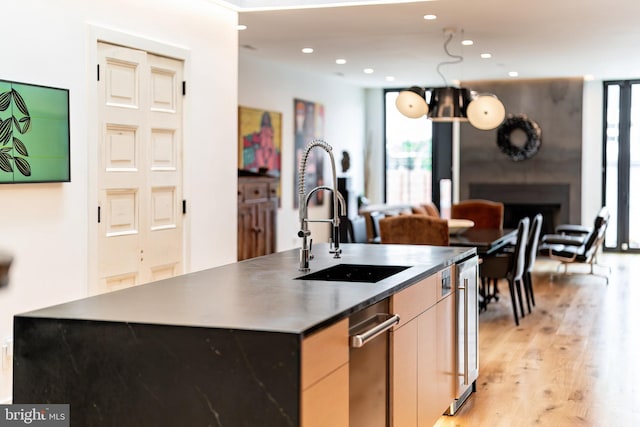 kitchen featuring light brown cabinetry, light wood-type flooring, sink, pendant lighting, and an island with sink