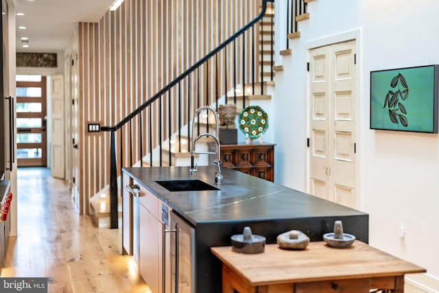 kitchen with sink, an island with sink, wine cooler, and light hardwood / wood-style flooring