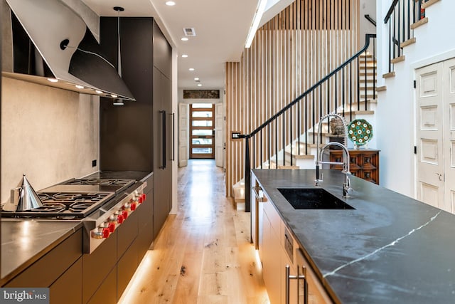 kitchen with wall chimney range hood, hanging light fixtures, sink, light wood-type flooring, and stainless steel gas cooktop