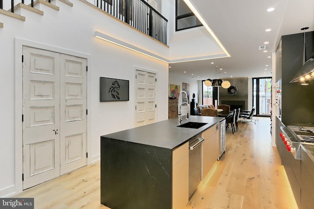 kitchen featuring stainless steel gas cooktop, a kitchen island with sink, sink, a high ceiling, and light hardwood / wood-style floors