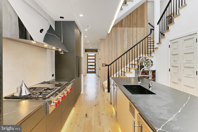 kitchen with stainless steel counters, sink, stainless steel gas cooktop, light hardwood / wood-style flooring, and extractor fan