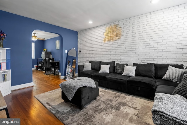 living room featuring hardwood / wood-style flooring, ceiling fan, and brick wall