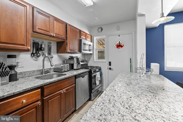 kitchen with appliances with stainless steel finishes, light tile patterned floors, pendant lighting, light stone countertops, and sink