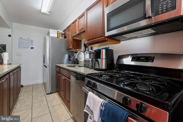 kitchen with stainless steel appliances, light tile patterned floors, light stone counters, and sink