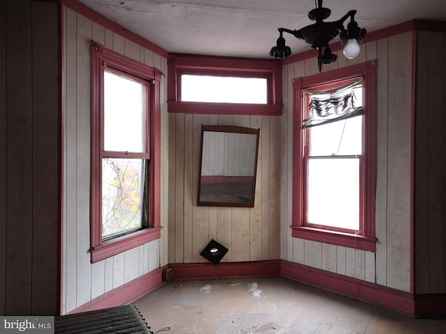 interior space with a healthy amount of sunlight, wooden walls, and a notable chandelier