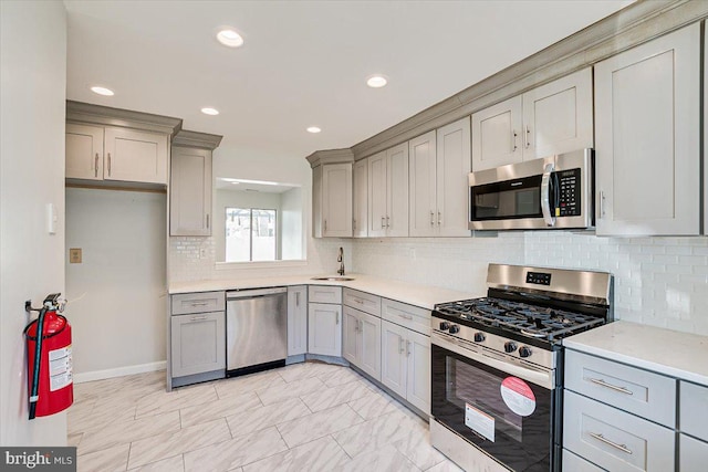 kitchen featuring sink, gray cabinets, backsplash, light stone countertops, and appliances with stainless steel finishes