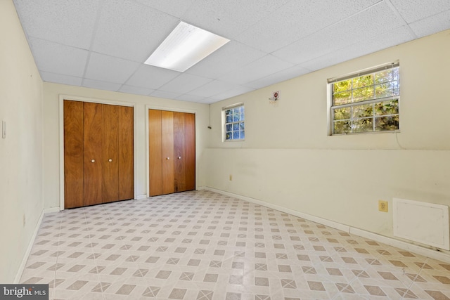 unfurnished bedroom featuring a paneled ceiling and multiple closets