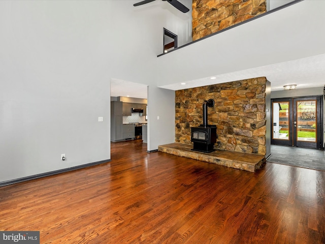 unfurnished living room with a wood stove, a high ceiling, french doors, ceiling fan, and wood-type flooring