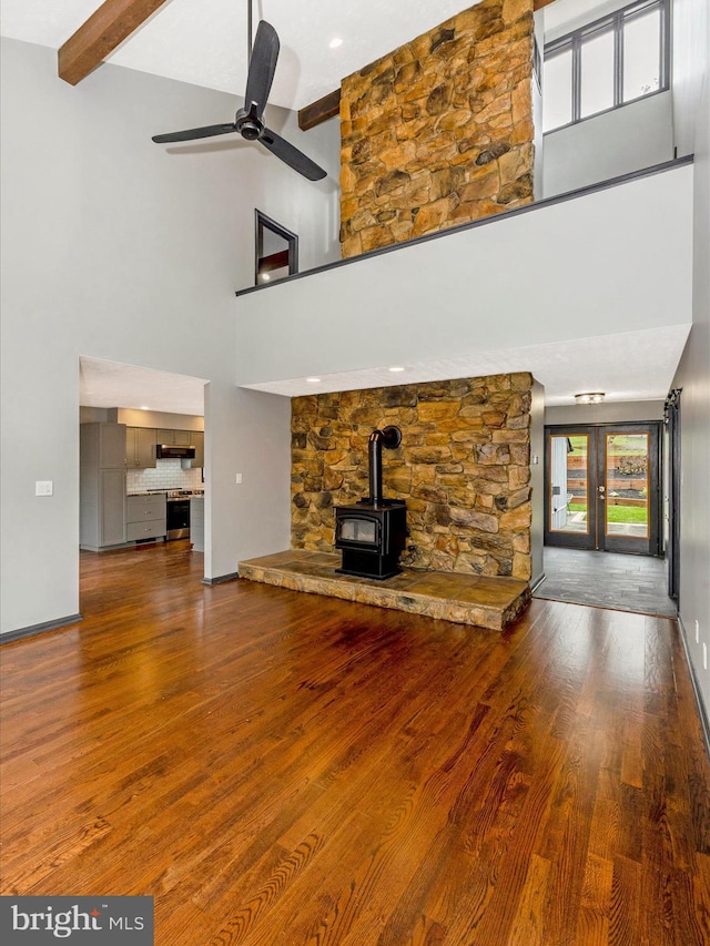 unfurnished living room featuring beam ceiling, a wood stove, ceiling fan, high vaulted ceiling, and hardwood / wood-style floors