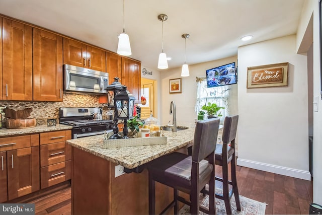 kitchen featuring appliances with stainless steel finishes, a kitchen breakfast bar, sink, decorative light fixtures, and light stone counters