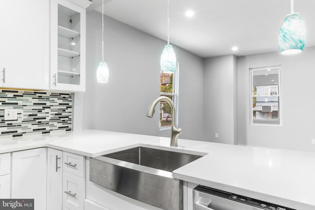 kitchen featuring decorative backsplash, stainless steel dishwasher, sink, pendant lighting, and white cabinetry