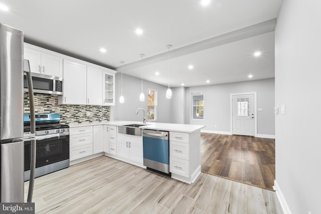 kitchen featuring white cabinetry, hanging light fixtures, stainless steel appliances, kitchen peninsula, and light wood-type flooring