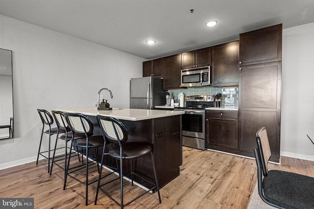 kitchen with sink, stainless steel appliances, a kitchen breakfast bar, tasteful backsplash, and light hardwood / wood-style flooring