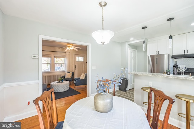 dining space featuring light hardwood / wood-style floors, ceiling fan, and radiator heating unit