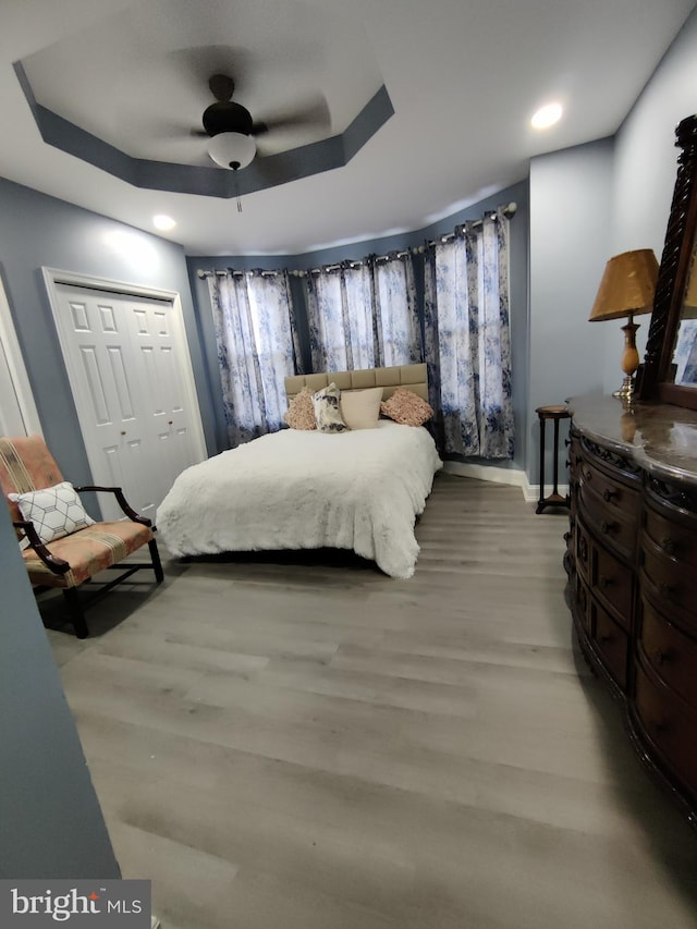 bedroom with ceiling fan, a closet, light wood-type flooring, and a raised ceiling