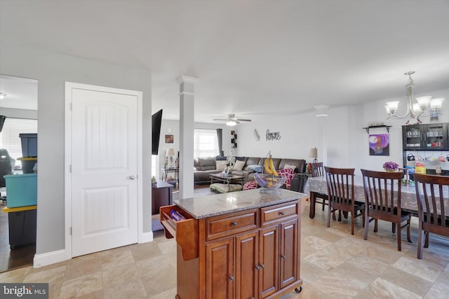 kitchen with a center island, decorative light fixtures, ceiling fan with notable chandelier, light stone counters, and decorative columns