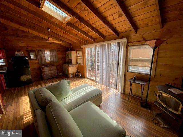 living room with hardwood / wood-style floors, vaulted ceiling with skylight, wooden walls, and wooden ceiling