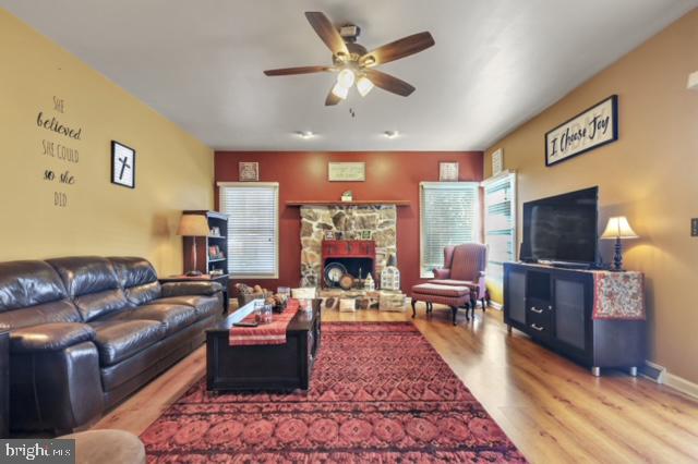 living room with a stone fireplace, ceiling fan, and light hardwood / wood-style floors