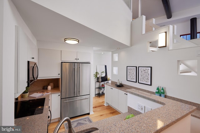 kitchen with light stone countertops, sink, light hardwood / wood-style flooring, white cabinets, and appliances with stainless steel finishes