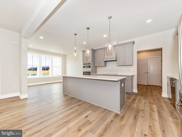 kitchen featuring gray cabinetry, light hardwood / wood-style flooring, backsplash, pendant lighting, and a center island with sink