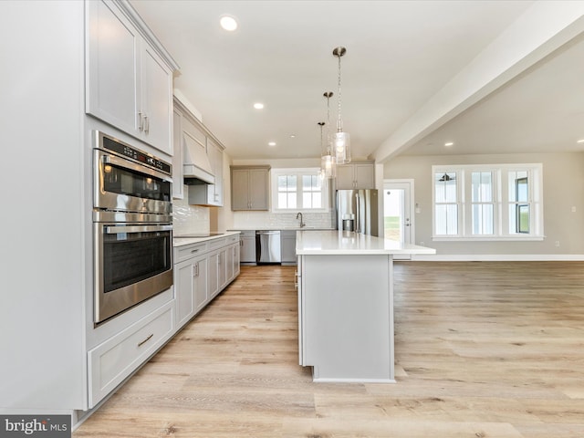 kitchen with decorative backsplash, appliances with stainless steel finishes, pendant lighting, a center island, and light hardwood / wood-style floors