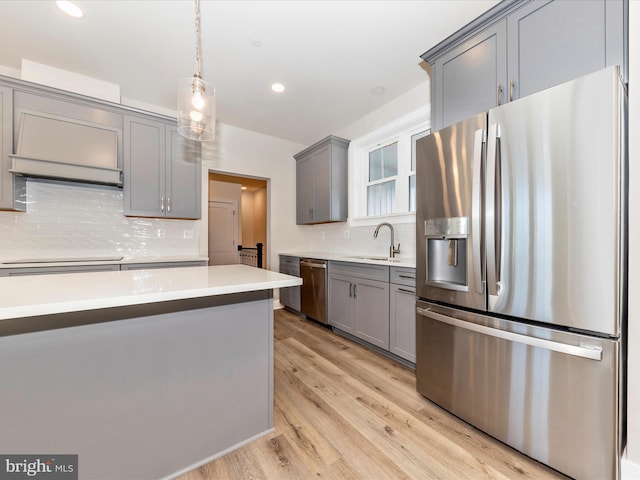 kitchen featuring gray cabinetry, sink, hanging light fixtures, appliances with stainless steel finishes, and light hardwood / wood-style floors