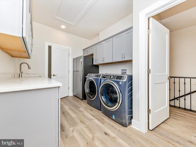 clothes washing area with light hardwood / wood-style floors, cabinets, separate washer and dryer, and sink