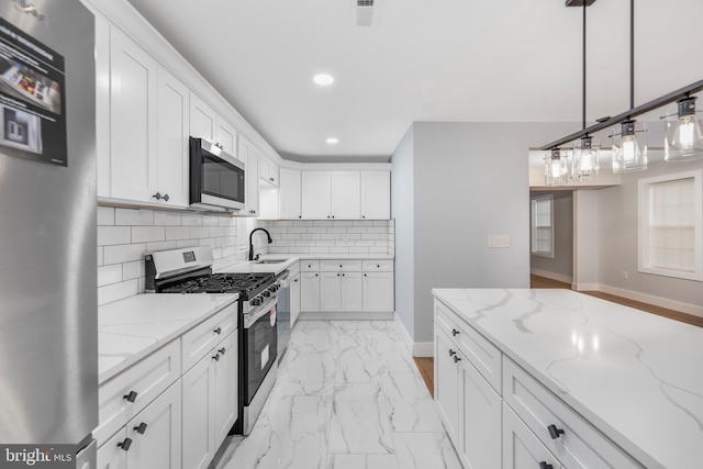 kitchen featuring white cabinetry, appliances with stainless steel finishes, light stone counters, and hanging light fixtures