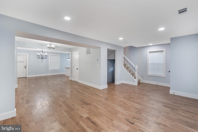 unfurnished living room with light wood-type flooring and an inviting chandelier