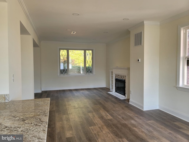 unfurnished living room featuring dark wood-type flooring, a high end fireplace, a healthy amount of sunlight, and ornamental molding