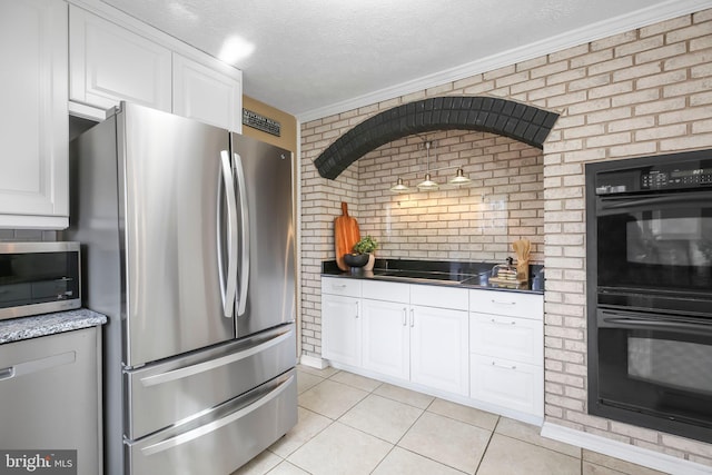 kitchen featuring light tile patterned floors, brick wall, black appliances, white cabinets, and a textured ceiling