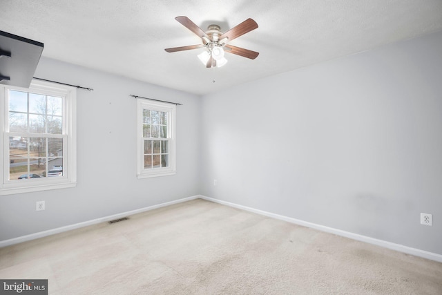 carpeted spare room featuring visible vents, a ceiling fan, and baseboards