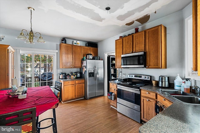 kitchen featuring stainless steel appliances, hardwood / wood-style floors, a notable chandelier, sink, and pendant lighting