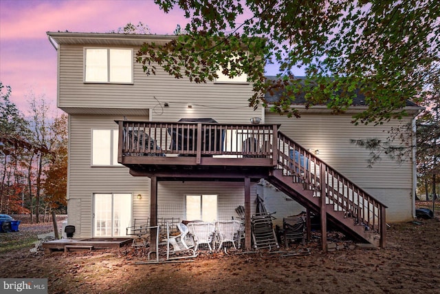 back house at dusk featuring a wooden deck and a patio area