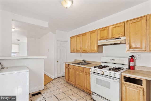 kitchen featuring sink, light tile patterned floors, washer and clothes dryer, gas range gas stove, and light brown cabinets