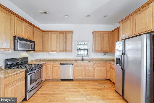 kitchen with light stone countertops, sink, light hardwood / wood-style floors, and appliances with stainless steel finishes