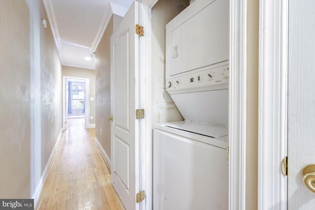 laundry room with crown molding, stacked washing maching and dryer, and light wood-type flooring