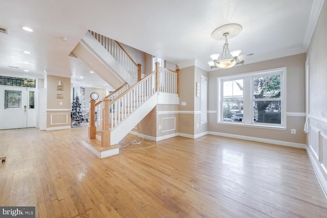 unfurnished living room featuring crown molding, an inviting chandelier, and light wood-type flooring