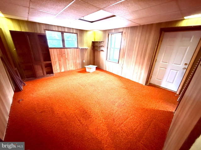 basement with a paneled ceiling, carpet, and wooden walls