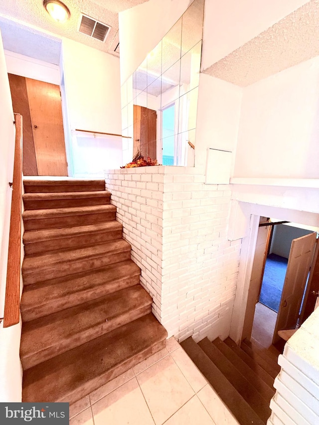 stairway featuring a textured ceiling, tile patterned flooring, and brick wall