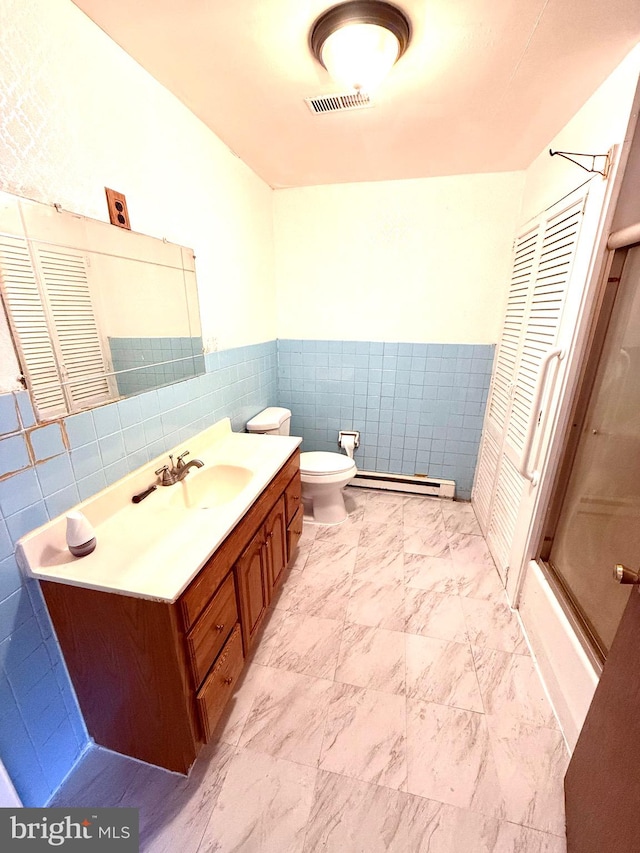 full bathroom with vanity, a baseboard heating unit, bath / shower combo with glass door, toilet, and tile walls