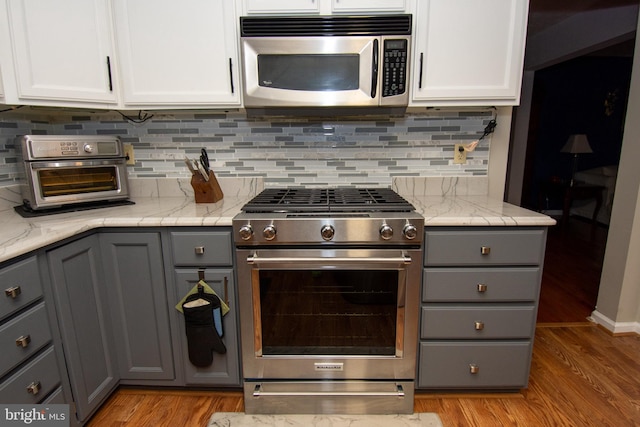 kitchen with gray cabinetry, white cabinets, light wood-type flooring, and appliances with stainless steel finishes