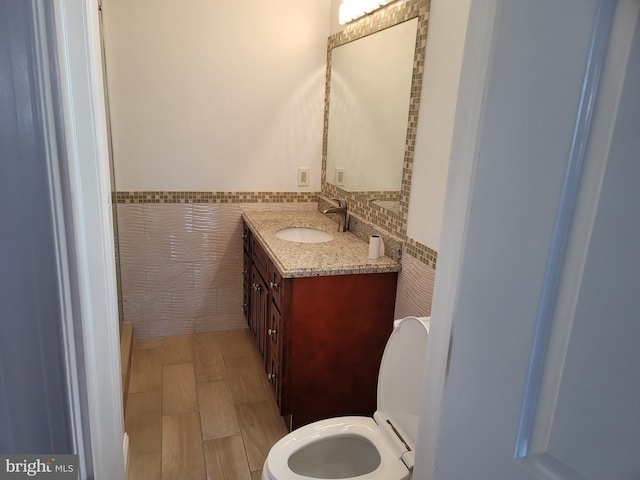 bathroom with a wainscoted wall, vanity, tile walls, and toilet
