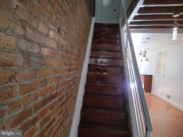 staircase with brick wall and hardwood / wood-style flooring