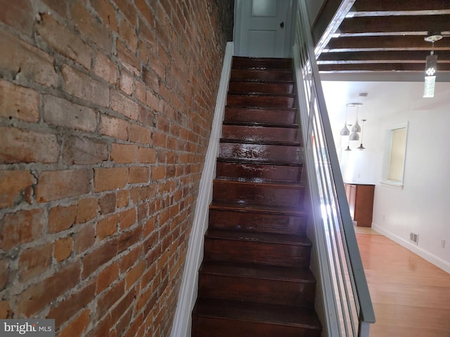 stairs with baseboards, wood finished floors, and brick wall