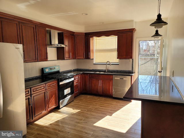 kitchen with hardwood / wood-style floors, wall chimney exhaust hood, sink, appliances with stainless steel finishes, and decorative light fixtures