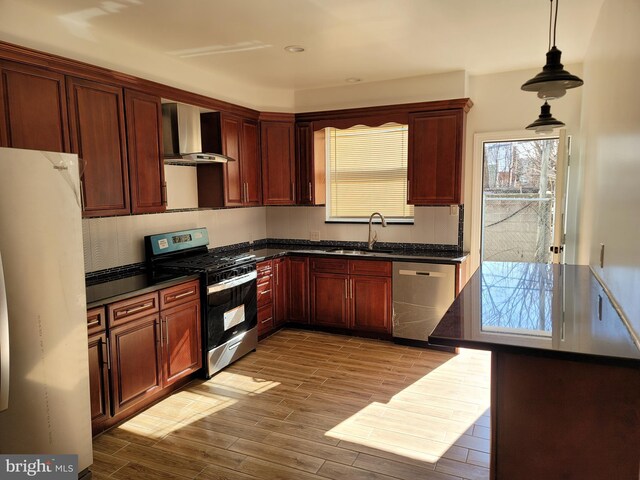 kitchen featuring wall chimney exhaust hood, stainless steel appliances, a sink, dark countertops, and wood finished floors