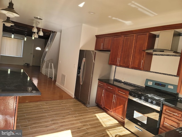 kitchen with wall chimney range hood, light hardwood / wood-style flooring, appliances with stainless steel finishes, and decorative light fixtures