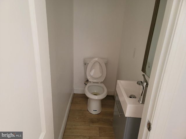 bathroom with toilet, baseboards, wood finished floors, and vanity