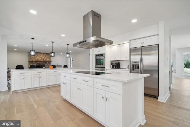 kitchen with kitchen peninsula, island exhaust hood, white cabinetry, appliances with stainless steel finishes, and decorative light fixtures